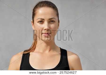 Athletic Motivated Woman With Pony Tail, Healthy Skin, Dressed In Black T Shirt, Looks Directly At C