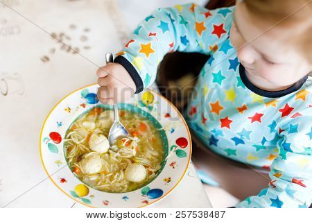 Adorable Baby Girl Eating From Spoon Vegetable Noodle Soup. Food, Child, Feeding And Development Con