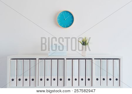 Modern Bright Business Office Interior Detail Depicting Wall Clock And Shelf With Books, Plant And F