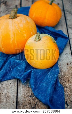 Close-up Of Three Orange Pumpkins On Vintage Wooden Background And Blue Towel