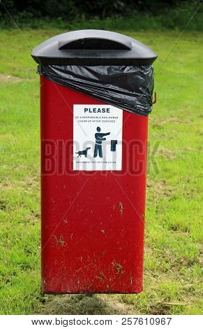 Red Dog Litter Bin On A Metal Pole Seen From The Front With Advisory Sticker And Hinged Black Lid In