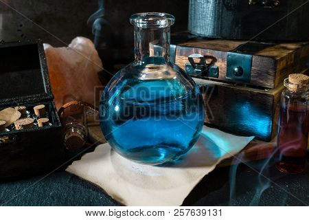 Magic Concept. Blue Potion In Bottle, Candles, Wooden Box And Craft Paper. Magical Background