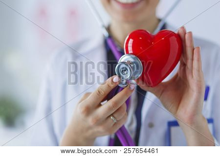 A doctor with stethoscope examining red heart, isolated on white background