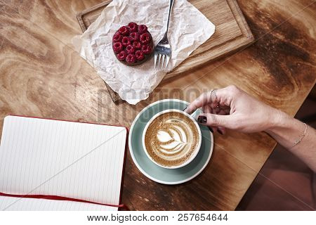 Cup Of Coffee Latte On Wooden Table Or Background In Woman Hands From Above. Having Lunch In Cafe. O