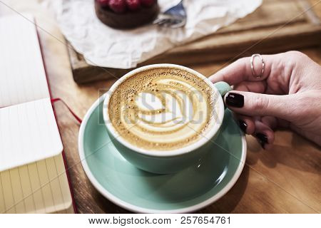 Close-up Cup Of Coffee Latte On Wooden Table In Woman Hands From Above. Having Lunch In Cafe.