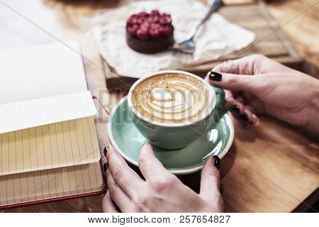 Cup Of Coffee Latte On Wooden Table Or Background In Woman Hands From Above. Having Lunch In Cafe. O