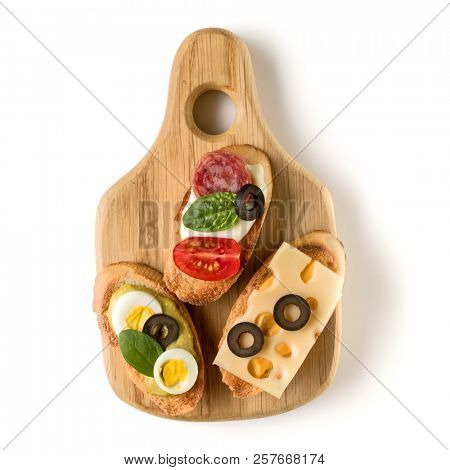 Open faced sandwich canape or crostini on a wooden serving board isolated on white background closeup. Top view.