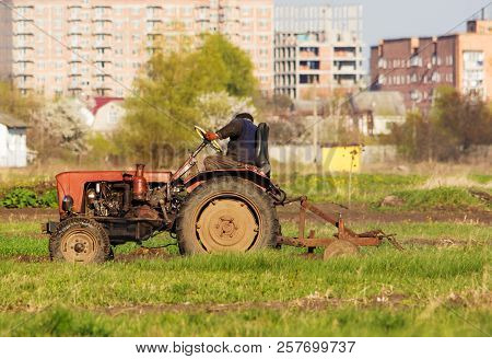 A Tractor Driver Plowing Soil In Autumn To Sow Winter Wheat. Side View Of A Tractor Driver On Tracto
