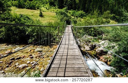 Wooden Hanging Bridge Leading Forward Over Green Mountain River.