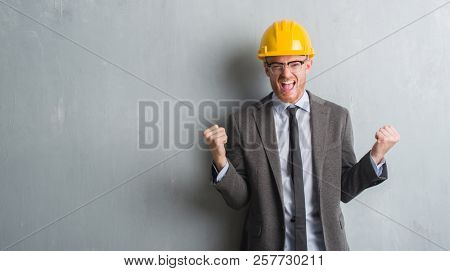 Young redhead man wearing architect outfit and helment screaming proud and celebrating victory and success very excited, cheering emotion
