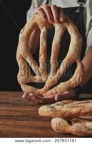 Baker lays freshly baked fougas bread on a wooden brown table