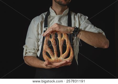 On a black background organic fresh fougas bread in the hands of a man