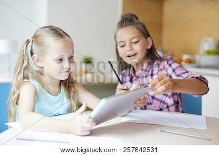 One of cute girls watching vid in touchpad while her sister paying attention to what is on screen