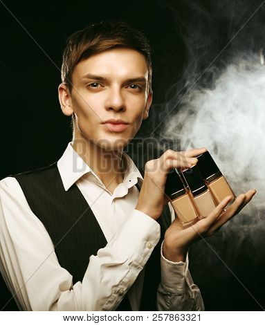 Young male make up artist posing with foundation for make-up on a dark background.