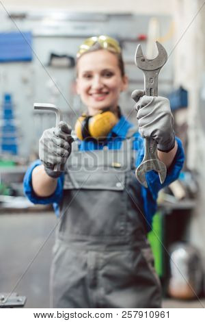 Woman mechanic showing tools to the camera holding wrench in her hand