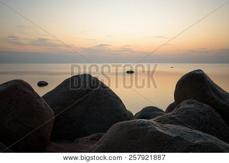 Large Stones On The Background Of The Sea At Sunset Tonted With Orange. Soft Focus.