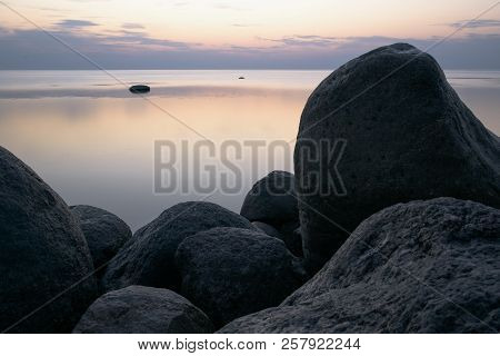 Large Stones On The Background Of The Sea At Sunset Tonted With Purple.