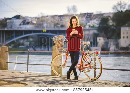 Theme Tourism On Bicycle And Modern Technology. Beautiful Young Caucasian Woman Stands Near Red Retr