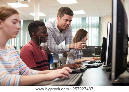 Teacher Helping Male High School Student Working In Computer Class