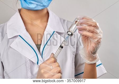 Fimale Doctor Injecting Syringe Into A Vial Bottle With Medicine. Isolated On Grey Backround.