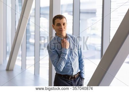 A 35-40 Year Old Man In A Blue Shirt Poses In The Office Back Hallway Against The Background Of A La