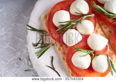 Toasts With Mozzarella, Tomatoes And Rosemary In A White Plate