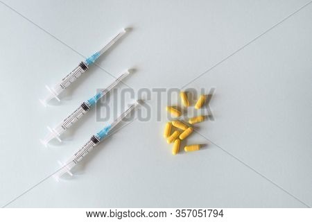 Three Syringes In A Row Lie Next To A Handful Of Yellow Capsules On A Light Background For Your Medi
