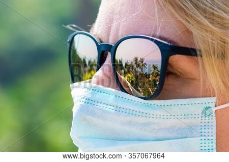 Travel And Healthcare Concept. Woman Wearing Medicine Mask And Sun Glasses With Tropical Resort Refl