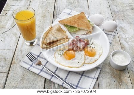 Breakfast Of Scrambled Eggs With Bacon, Pancakes, Sandwich And Orange Juice. On A Wooden Table