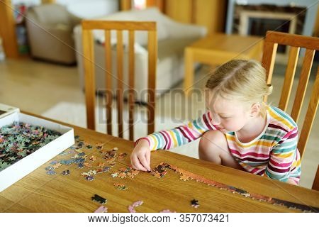 Cute Young Girl Playing Puzzles At Home. Child Connecting Jigsaw Puzzle Pieces In A Living Room Tabl