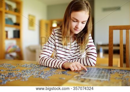 Cute Young Girl Playing Puzzles At Home. Child Connecting Jigsaw Puzzle Pieces In A Living Room Tabl