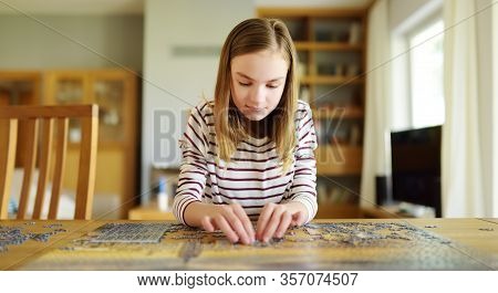 Cute Young Girl Playing Puzzles At Home. Child Connecting Jigsaw Puzzle Pieces In A Living Room Tabl