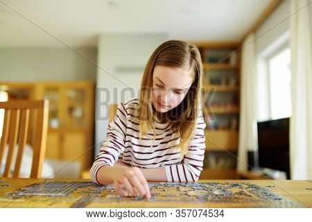 Cute Young Girl Playing Puzzles At Home. Child Connecting Jigsaw Puzzle Pieces In A Living Room Tabl
