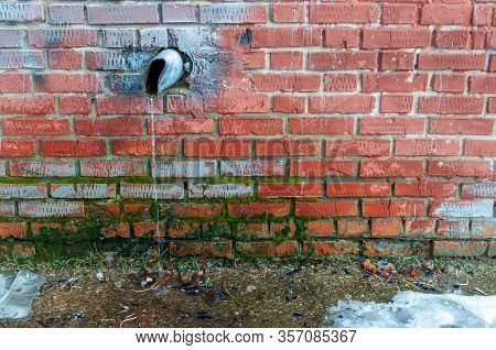 Water Running Down An Old Battered Water Pipe Onto The Melting Snow