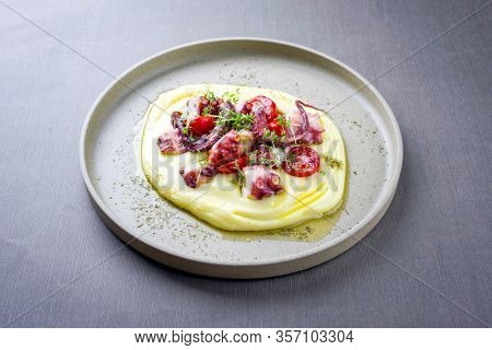 Traditional Italian polpo alla griglia su crema di patate with barbecued octopus, potato creme and tomatoes as closeup on a modern design plate 