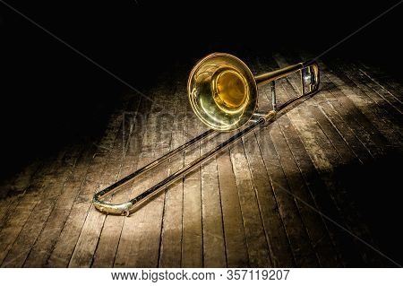 Golden Brass Instrument Trombone Lies On A Dark Brown Wooden Stage In The Rays Of Light
