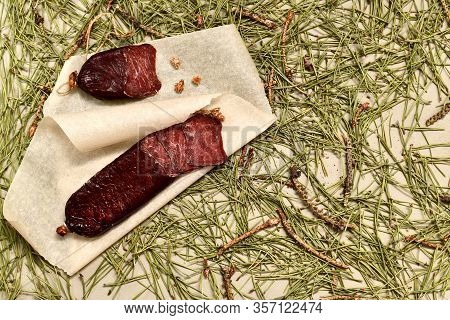 Dried Sausage Made Of Roe Meat Cut With Slices On Parchment With Pine Buds On The Left Flooring Made
