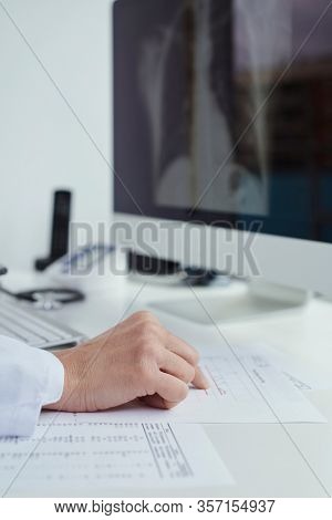 closeup of a young doctor man, wearing a white coat, sitting at his desk checking a chest radiograph in his computer