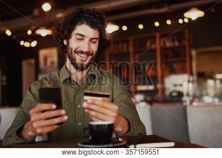Happy Caucasian Bearded Man Holding Mobile Phone Typing Card Data To Make Online Payment Sitting In 