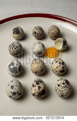Quail Eggs On White Plate. One Egg Is Broken, The Yellow Yolk Leaked.