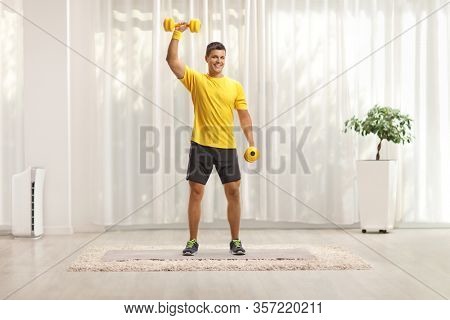 Full length portrait of a man exercising with weigths at home