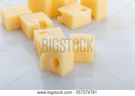 Portions (cubes, Dice) Of Emmental Swiss Cheese. Texture Of Holes And Alveoli. On White Marble Backg