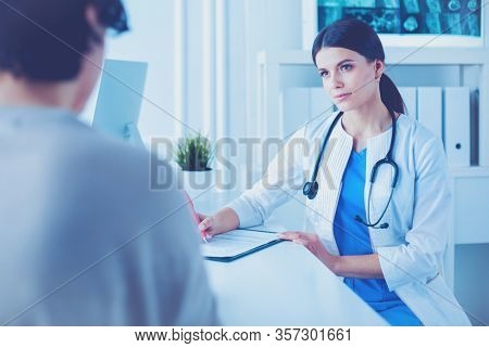 Doctor and patient discussing medical problems in a hospital consulting room. Doc filling in a patient's form