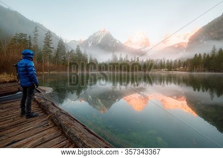 Man Standing At A Mountain Lake Enjoying The Sunrise In The Austrian Alps