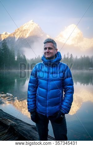 Man Standing At A Mountain Lake Enjoying The Sunrise In The Austrian Alps