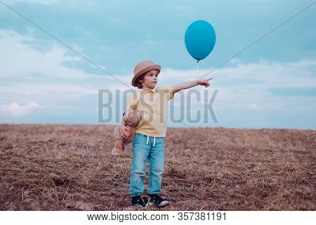 Little Boy On The Rural Road Between The Colored Groung Field Pointing At A Copyspace. The Cute Boy 