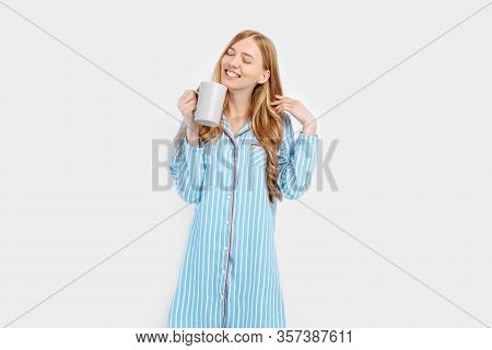 Beautiful Girl In Striped Pajamas, With A Cup In Her Hands , Drinking Coffee Or Tea In The Early Mor