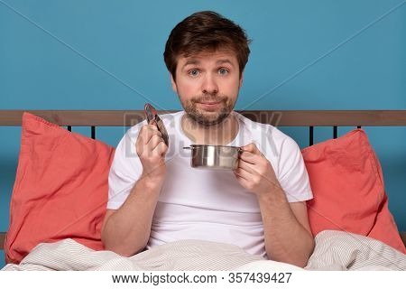 Sad Man In Bed Eating A Tasteless Soup With A Disgruntled Look.