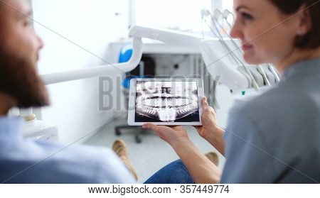 Rear View Of Dentist Talking To Man In Dentist Surgery, A Dental Check-up.