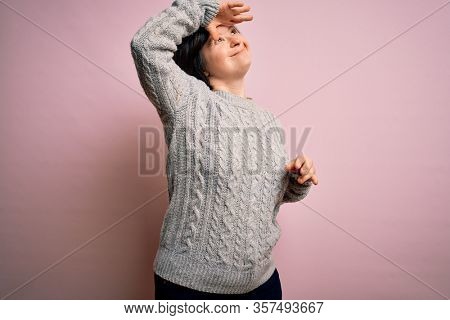 Young down syndrome woman wearing casual sweater over isolated background very happy and smiling looking far away with hand over head. Searching concept.